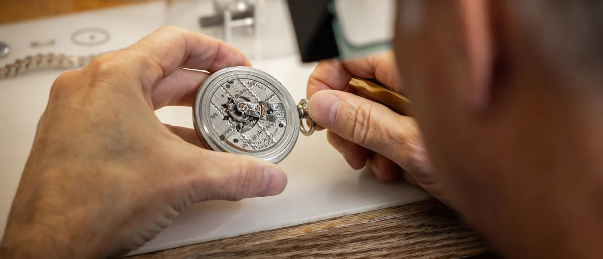 Person holding a pocket watch with intricate mechanisms on a wooden surface